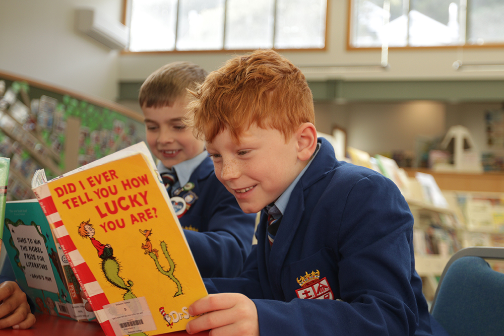 Two students wearing Wellesley College blazers reading books in the library