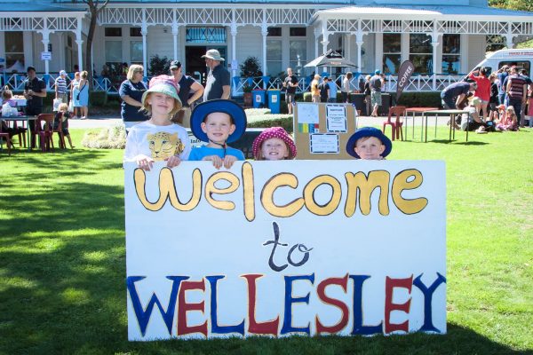 Four children in front of Days Bay House holding a ‘Welcome to Wellesley’ sign