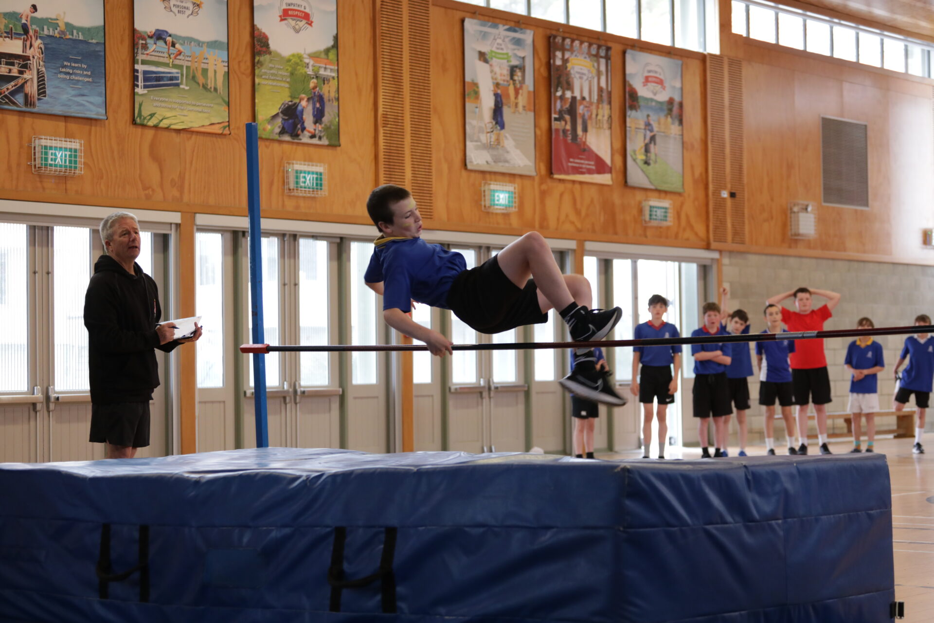 A boy in the Wellesley College hall clears the bar, focused on his jump during a sports activity