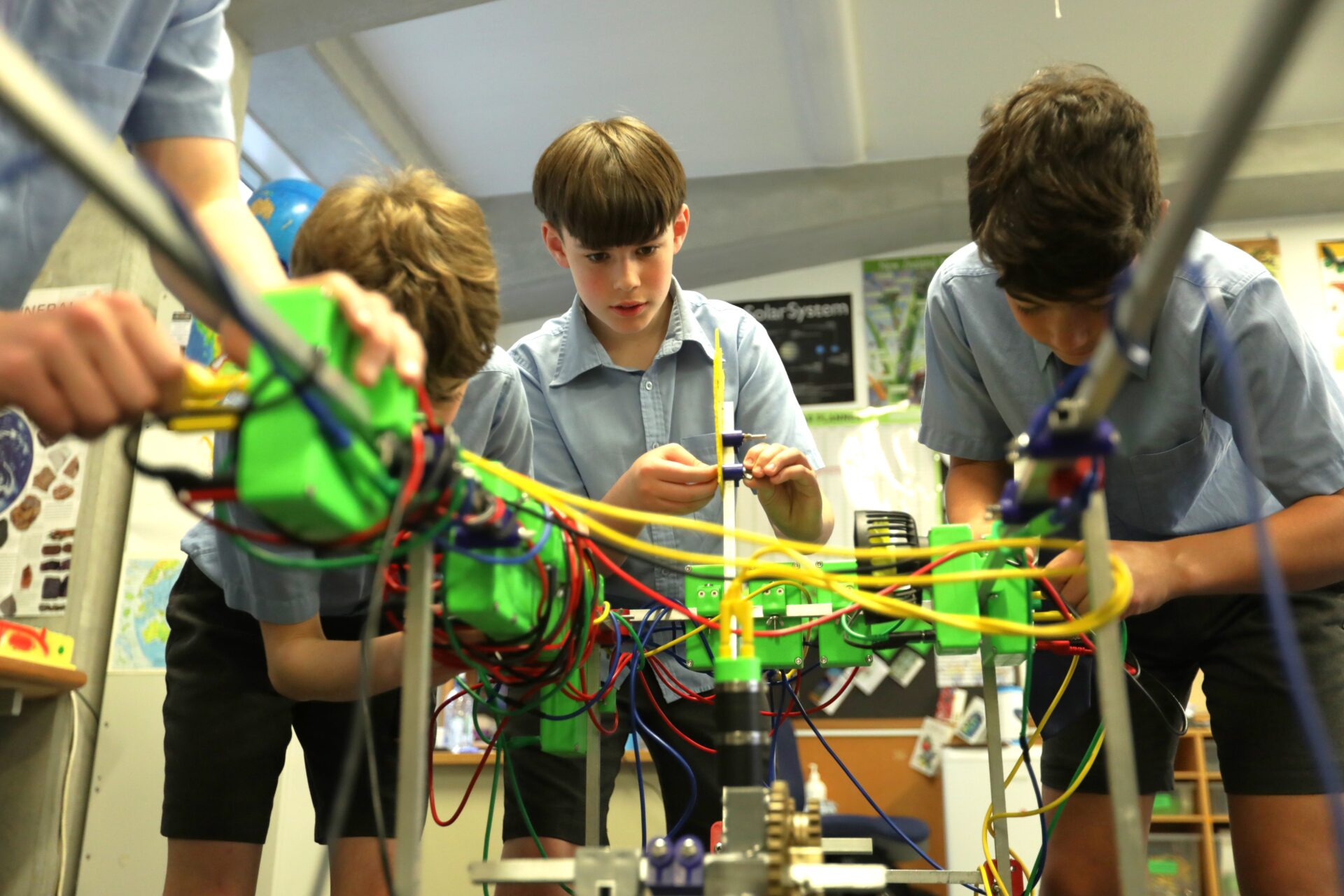 "Three boys in school uniforms work together on a colorful, complex EPRO8 project with wires and components in a classroom setting"