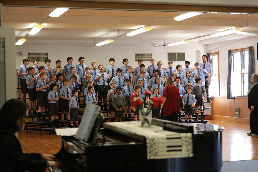 A group of Wellesley College boys stand together singing in the school choir, dressed in uniform and performing with focus and enthusiasm