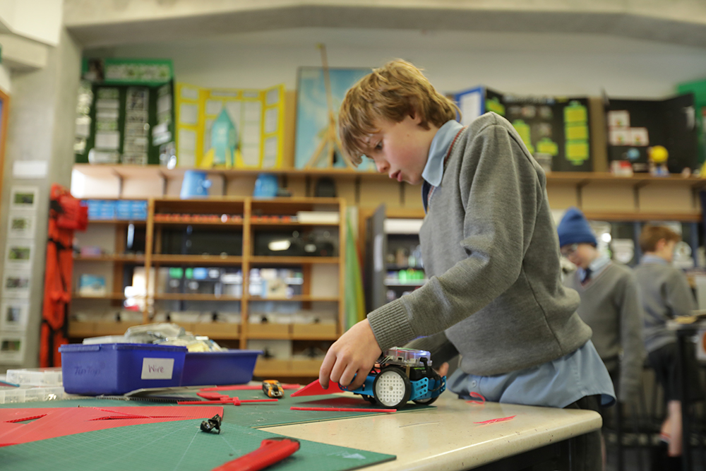 A student works on a robotics project in the STEM room, carefully assembling components on a workbench surrounded by tools and equipment