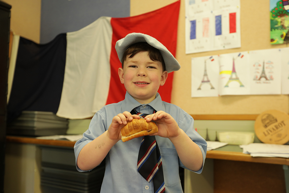 A student at Wellesley College learning French, holding a crepe and smiling at the camera