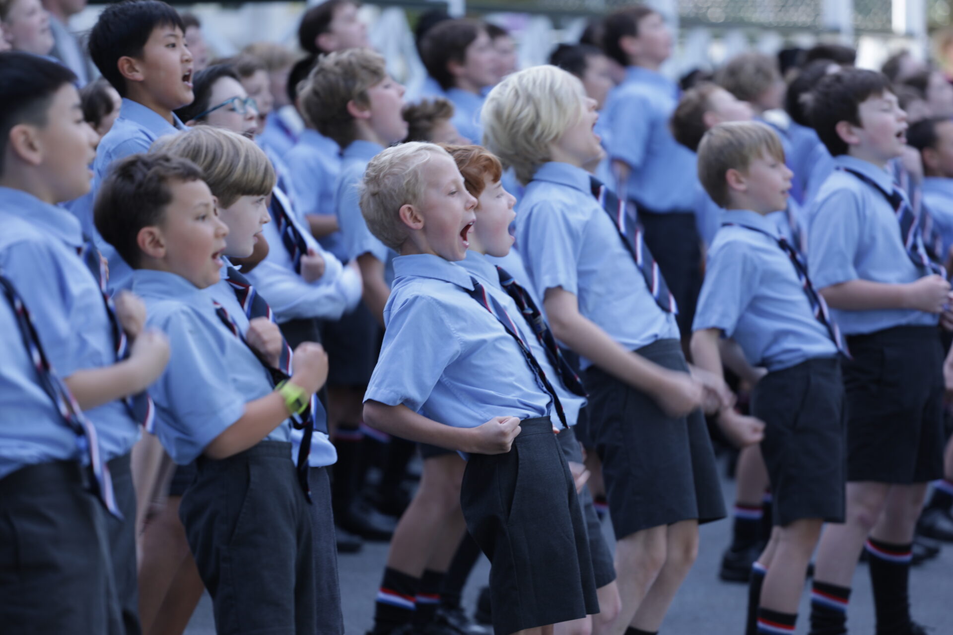 A group of Wellesley College boys performing the haka outdoors, standing in formation with intense expressions and strong, synchronised movements, wearing school uniforms