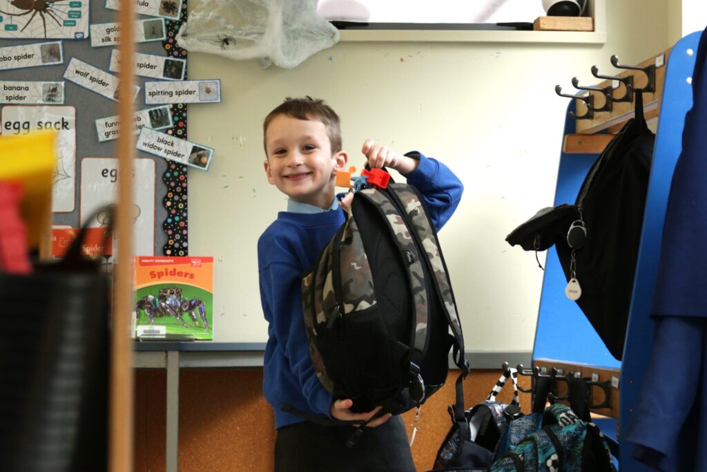 Young boy in school uniform holding his bag and smiling