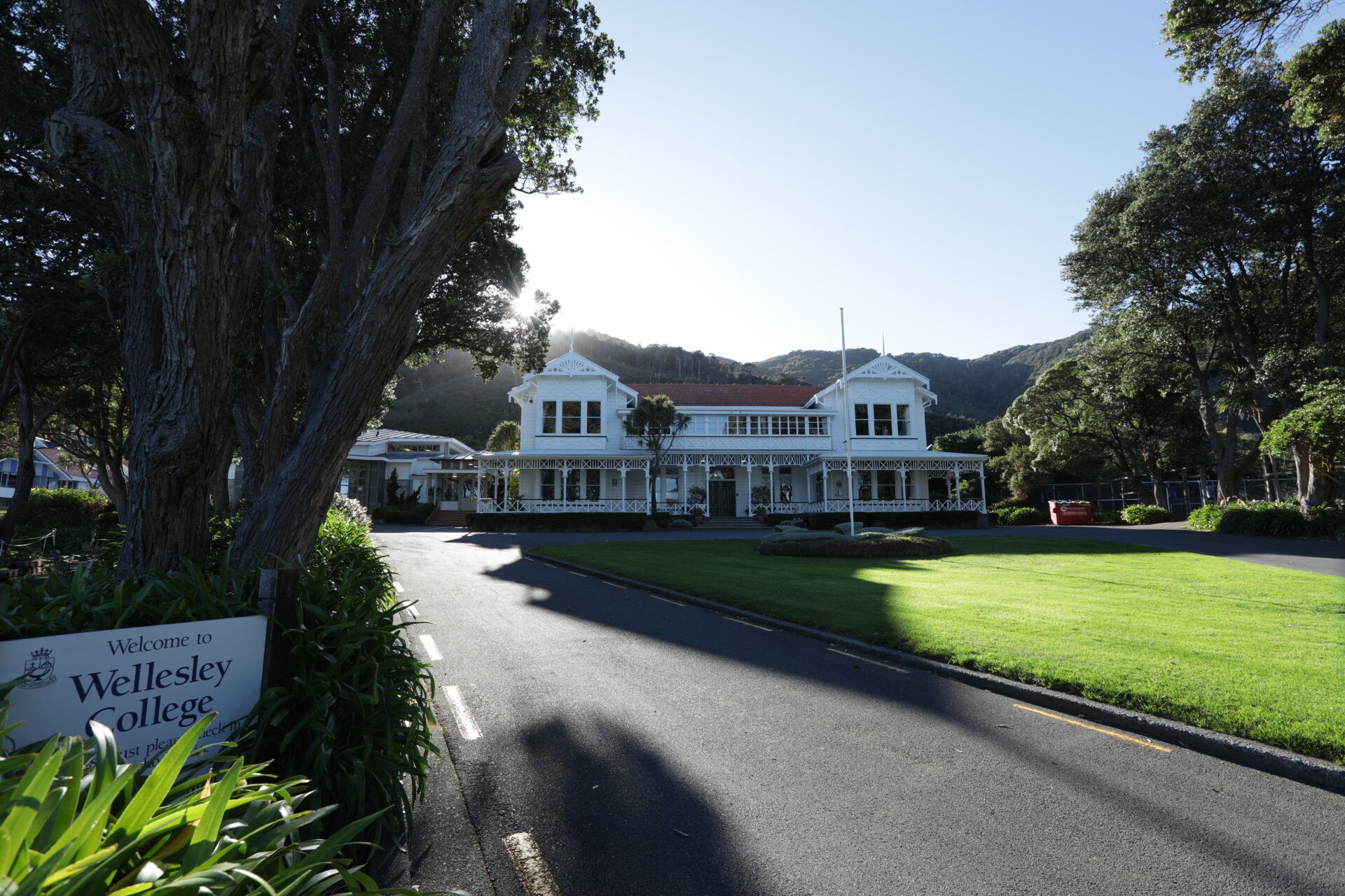 Days Bay House, surrounded by green lawns and trees. A sign in the foreground reads Wellesley College. The scene is bright and sunny